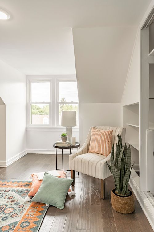 Attic bonus room with a sloped ceiling, striped armchair and a colorful kilim-style rug