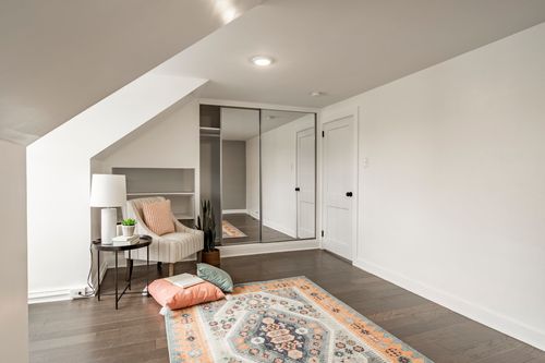 Attic bedroom with mirrored closet doors, a striped armchair and a colorful patterned rug