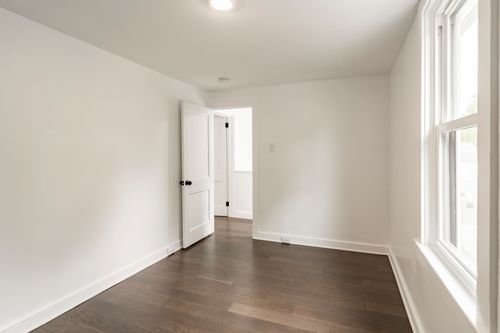 Empty bedroom with hardwood floors and a doorway open to the hallway