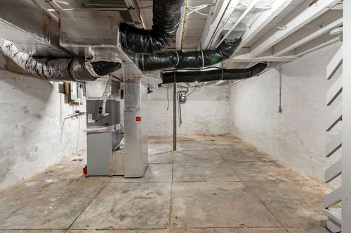 Unfinished basement with exposed ductwork, a furnace and whitewashed stone walls