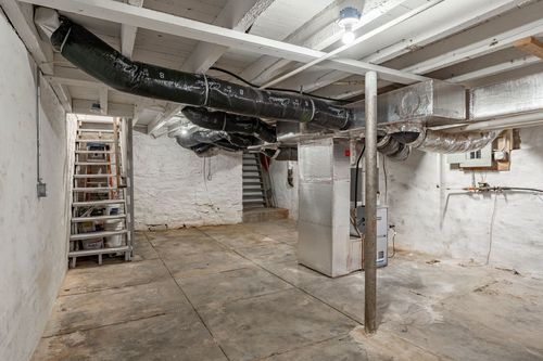 Unfinished basement with insulated ductwork, a wood ladder and a staircase in the background