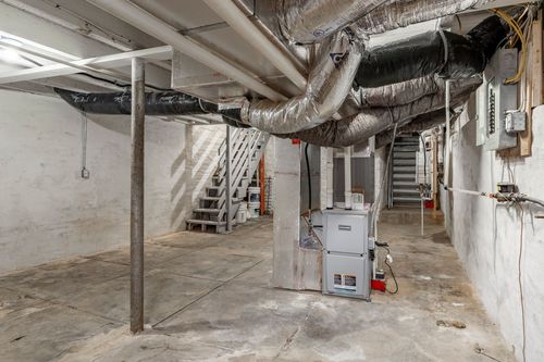 Unfinished basement with a furnace, wrapped ductwork and a staircase to the main floor