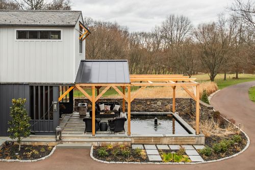 Aerial view of a timber-frame pavilion with a black standing-seam roof over a stone-edged reflecting pool