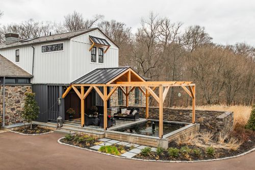 Aerial view of a timber pavilion with outdoor seating beside a modern farmhouse and pool