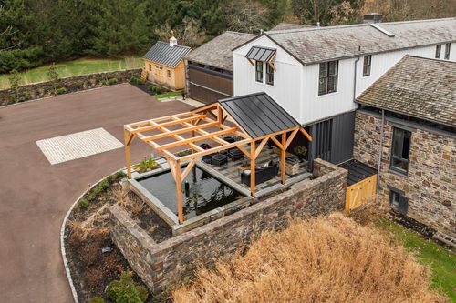 Aerial view of a timber pool pavilion beside a long driveway and a distant guest house