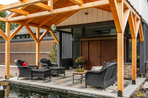 Under a timber pergola looking toward dark wood double doors and black wicker lounge seating