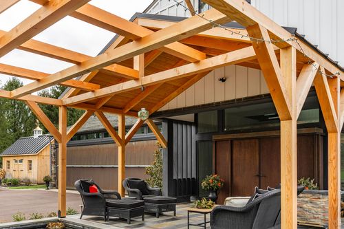 Exposed timber trusses and string lights over a stone patio with black wicker furniture