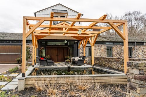 Timber pavilion over a reflecting pool facing dark wood double doors and a stone retaining wall