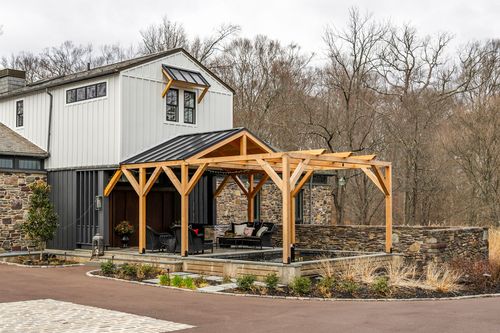 Cedar timber-frame pergola with wicker lounge seating attached to a white board-and-batten guest house