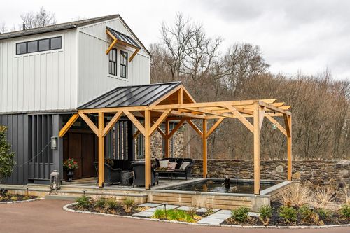 Timber-frame pavilion over a stone-edged reflecting pool beside a modern farmhouse