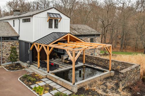 Aerial view of a timber-frame pool pavilion attached to a white board-and-batten home