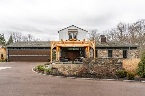 Stone and board-and-batten farmhouse with timber-frame entry portico and circular driveway