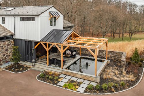 Aerial view of lounge seating beneath a timber pergola over a rectangular reflecting pool
