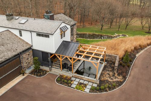 Wide aerial view of a farmhouse with timber pavilion, driveway and wooded hills beyond