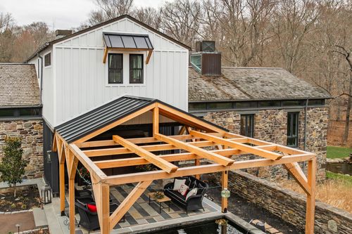 Aerial close-up of a timber-frame roof structure against a white board-and-batten house
