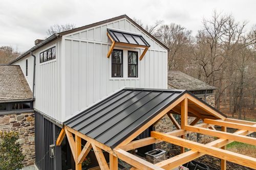 Angled exterior view of a white board-and-batten home with a black metal roof and timber pergola frame