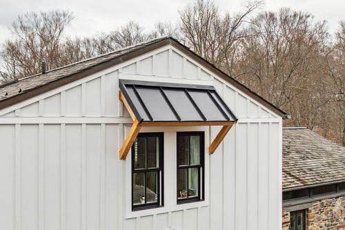 Close-up of a black standing-seam metal awning with timber brackets over black-framed windows