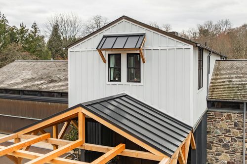 Aerial view of a gabled dormer with a metal awning above a timber-frame roof under construction