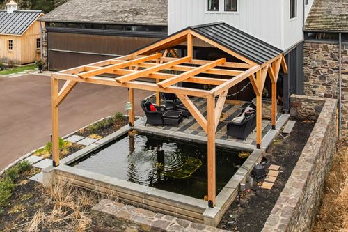 Aerial view of a timber pavilion with black roof and outdoor seating beside a garage and driveway