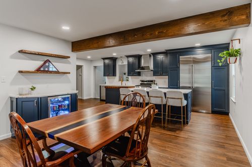 Open-concept dining and kitchen with a wood beam ceiling and navy island beyond a farmhouse table