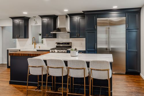 Navy blue kitchen with white oak floors, brass hardware and a stainless paneled refrigerator