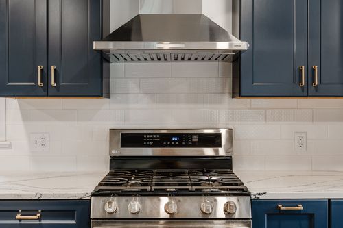 Gas range, stainless hood and walnut butcher-block island top in a navy kitchen