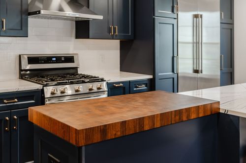 Navy kitchen with brass faucet, farmhouse sink and gas range along white subway tile