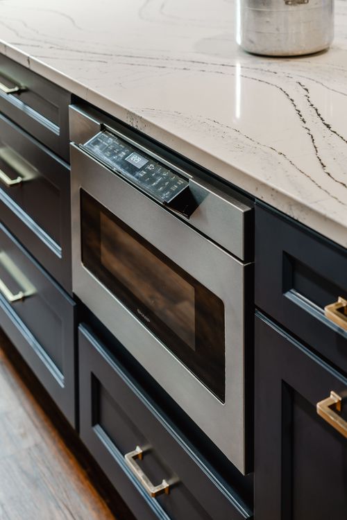 Crown-molded navy cabinets flank a brass faucet and farmhouse sink
