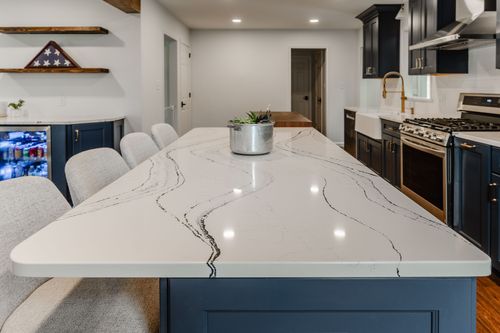 Navy kitchen island with brass barstools opens onto a paneled refrigerator wall