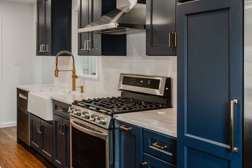Navy kitchen counter with a hallway view and brass faucet in the background