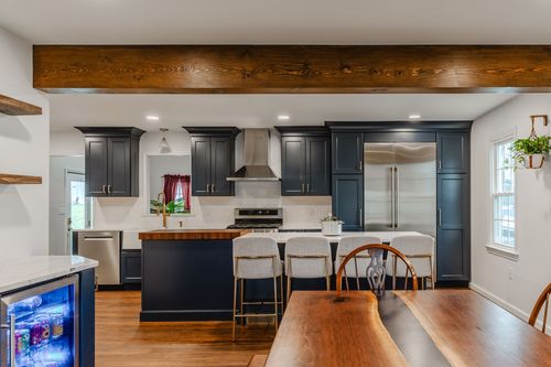 Farmhouse sink with a brass gooseneck faucet beneath a mirror and pendant light in a navy kitchen