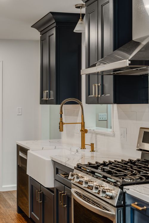 Brass faucet, farmhouse sink and gas range beneath crown-molded navy cabinets