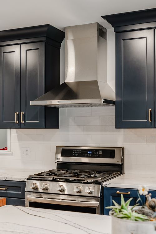 Close-up of a stainless range and hood between navy shaker cabinets