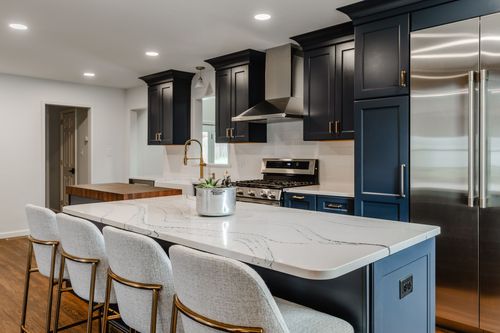 Navy kitchen island with brass barstools and paneled refrigerator wall