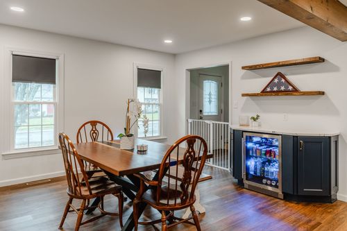 Farmhouse dining table with windsor chairs beside a built-in beverage bar