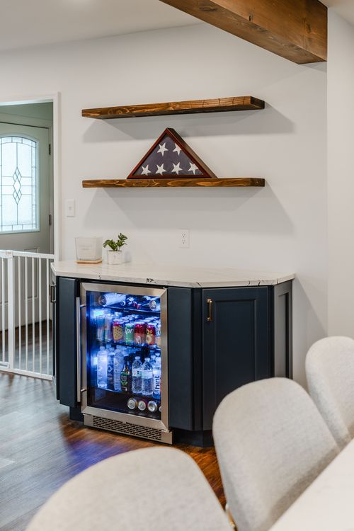 Built-in navy beverage fridge beneath floating wood shelves with a folded flag display