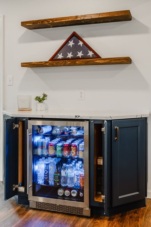 Open cabinet doors reveal a stocked beverage fridge beneath a flag shadow box