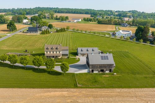 Aerial view of a stone farmhouse and matching bank barn with solar panels around a circular driveway