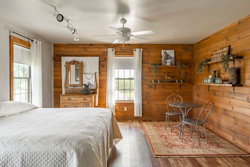 Knotty pine bedroom with a wrought iron bed, small bistro table and layered area rug