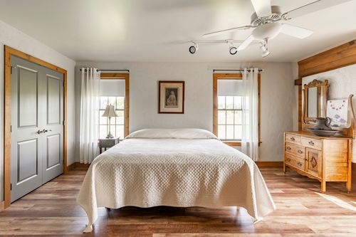 Bedroom with gray paneled doors, wood window trim and an antique dresser with mirror