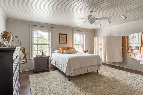 Bedroom with beadboard ceiling, dark wood dresser and a quilt rack against the wall