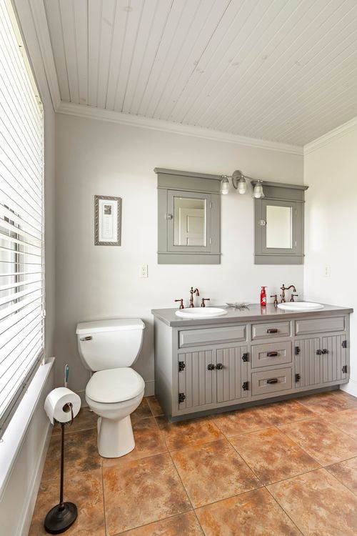 Bathroom with a gray double-sink vanity and warm-toned tile flooring
