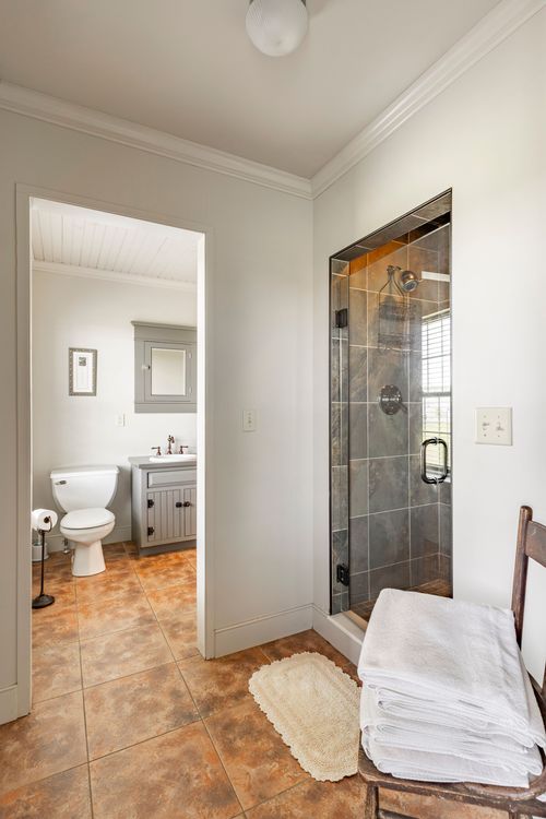 Hallway leading to a glass-enclosed shower with folded towels and a wood chair