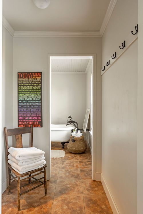 Hallway leading to a bathroom with a clawfoot tub, wicker baskets and coat hooks