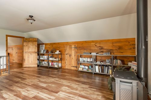 Vaulted loft room with wood plank walls, bookshelves and a wood stove
