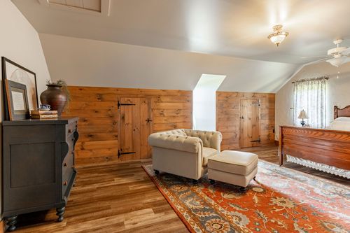 Loft bedroom with knotty pine barn doors, a dark dresser and tufted lounge chair
