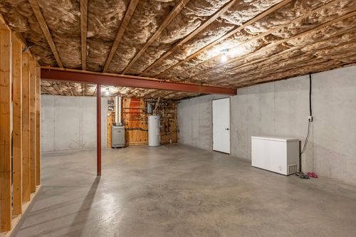 Unfinished basement with exposed insulation, a red support beam and chest freezer