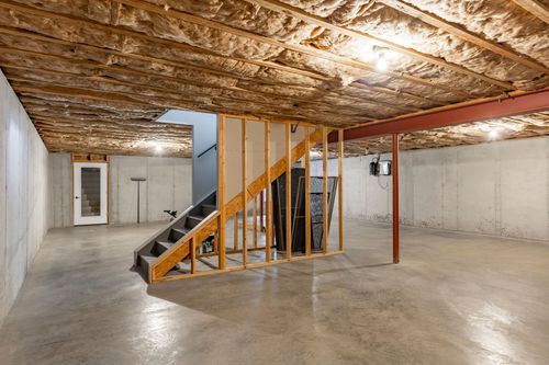 Unfinished basement with an open wood staircase and framed storage closet