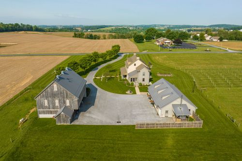 Aerial view of a farmhouse and barn beside a garden with an iron trellis walkway