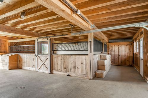 Barn aisle with a wood beam ceiling, horse stalls and concrete flooring